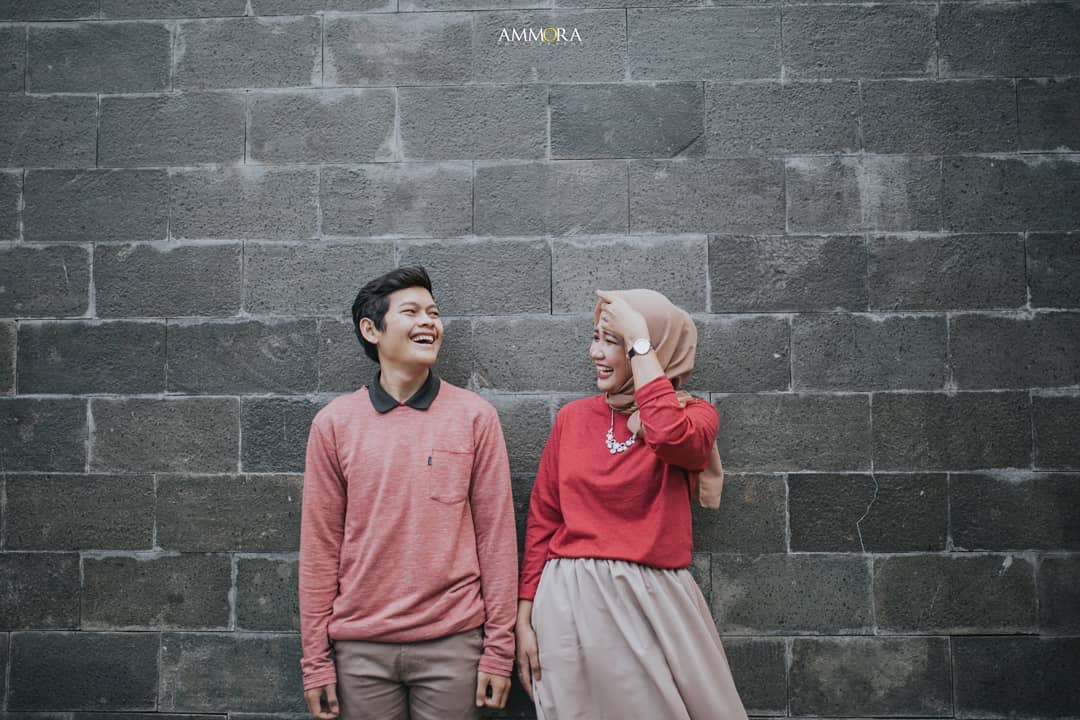 Seorang perempuan berfoto selfie di depan dinding estetik sebuah cafe dengan pencahayaan hangat.