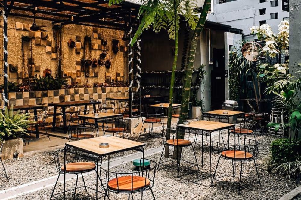 Kafe rumahan sederhana di gang kecil dengan suasana asri dan banyak tanaman hijau.