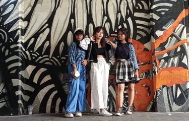 Remaja berfoto di depan mural dinding kafe yang artistik dan warna-warni.