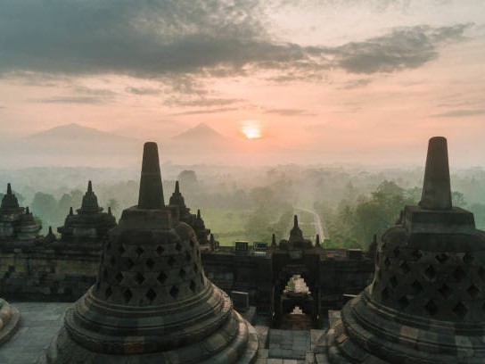 Gambar Candi Borobudur saat matahari terbit dengan pegunungan berkabut.