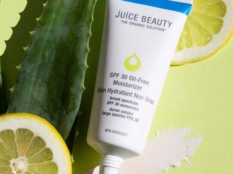 Gambar tube Juice Beauty SPF 30 Oil-Free Moisturizer dengan ilustrasi buah organik atau elemen botani alami, menonjolkan komposisi alami dan organiknya, dengan latar belakang samar Jakarta Selatan.