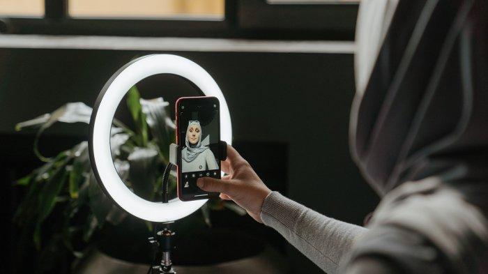 Seorang konten kreator sedang merekam video menggunakan smartphone dengan stabilizer.