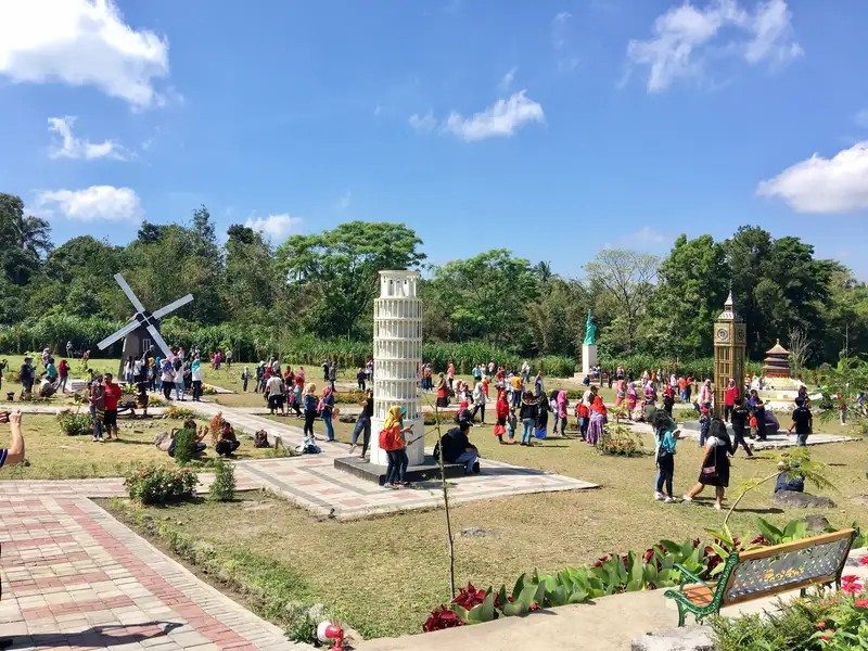 Gambar orang-orang berpose dengan miniatur landmark terkenal di Merapi Park.