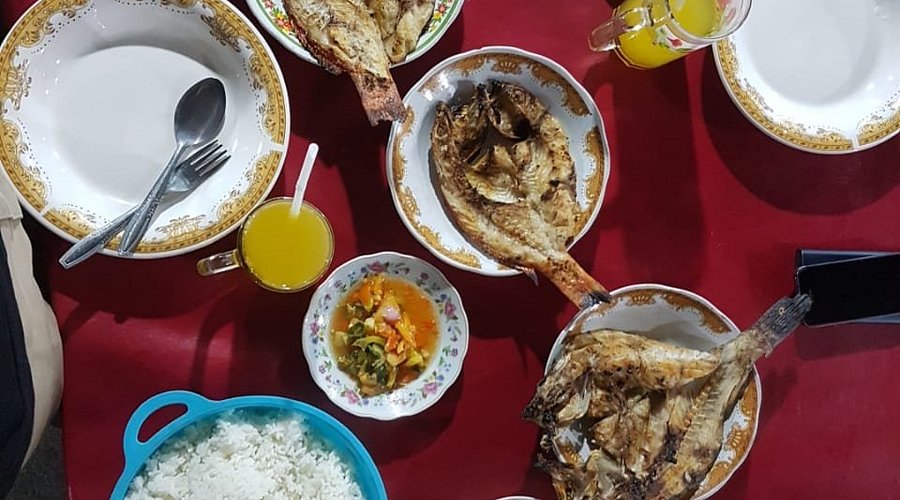 Piring berisi ikan bakar segar dengan sambal dan lalapan di atas meja restoran.