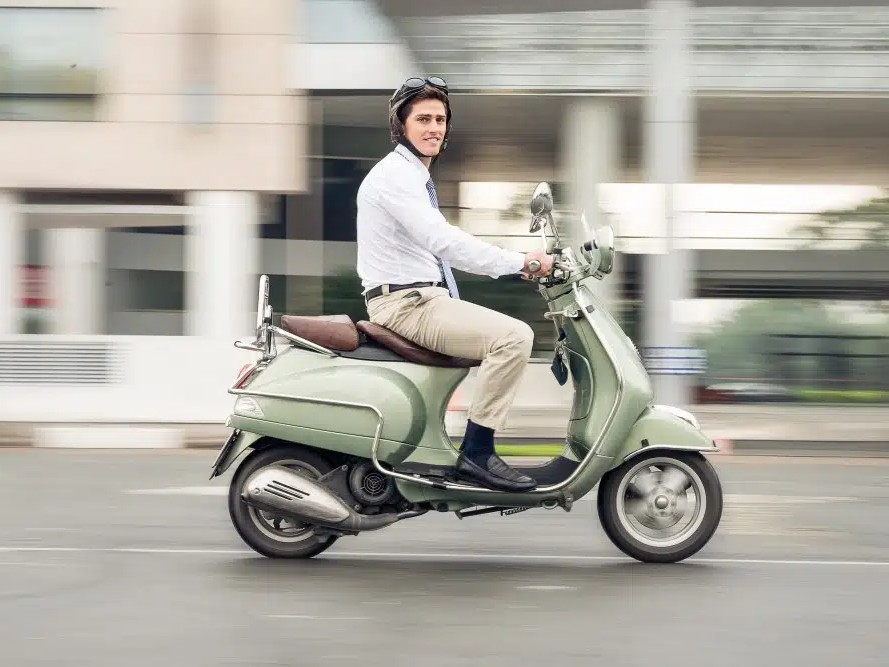Gambar toko skuter stylish yang menampilkan Vespa vintage dan skuter matic modern, dengan beberapa perlengkapan berkendara dan aksesoris dipajang.