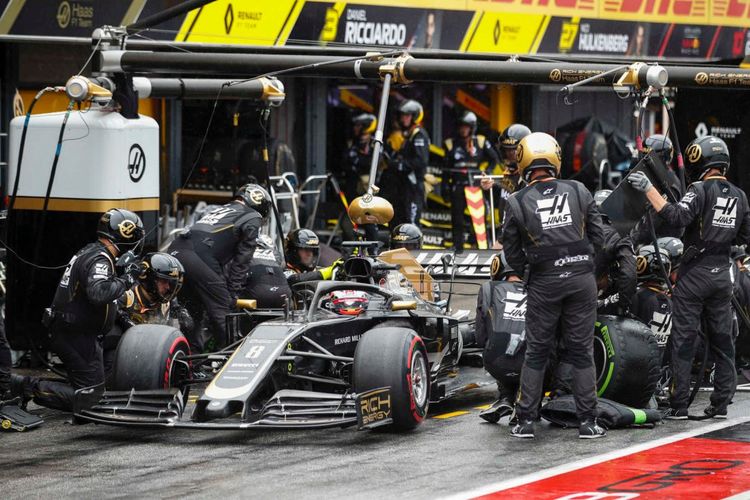 Mobil balap yang sedang dipanaskan di pit stop dengan mekanik bersiap di belakangnya.