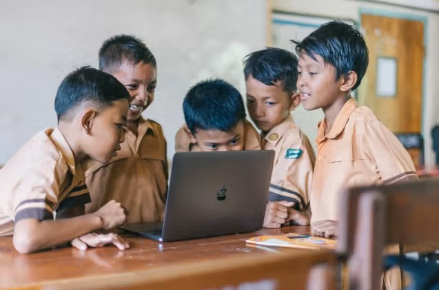 Gambar seorang siswa sedang membantu teman sekelompoknya menyelesaikan sebuah teka-teki kolaboratif di kelas.