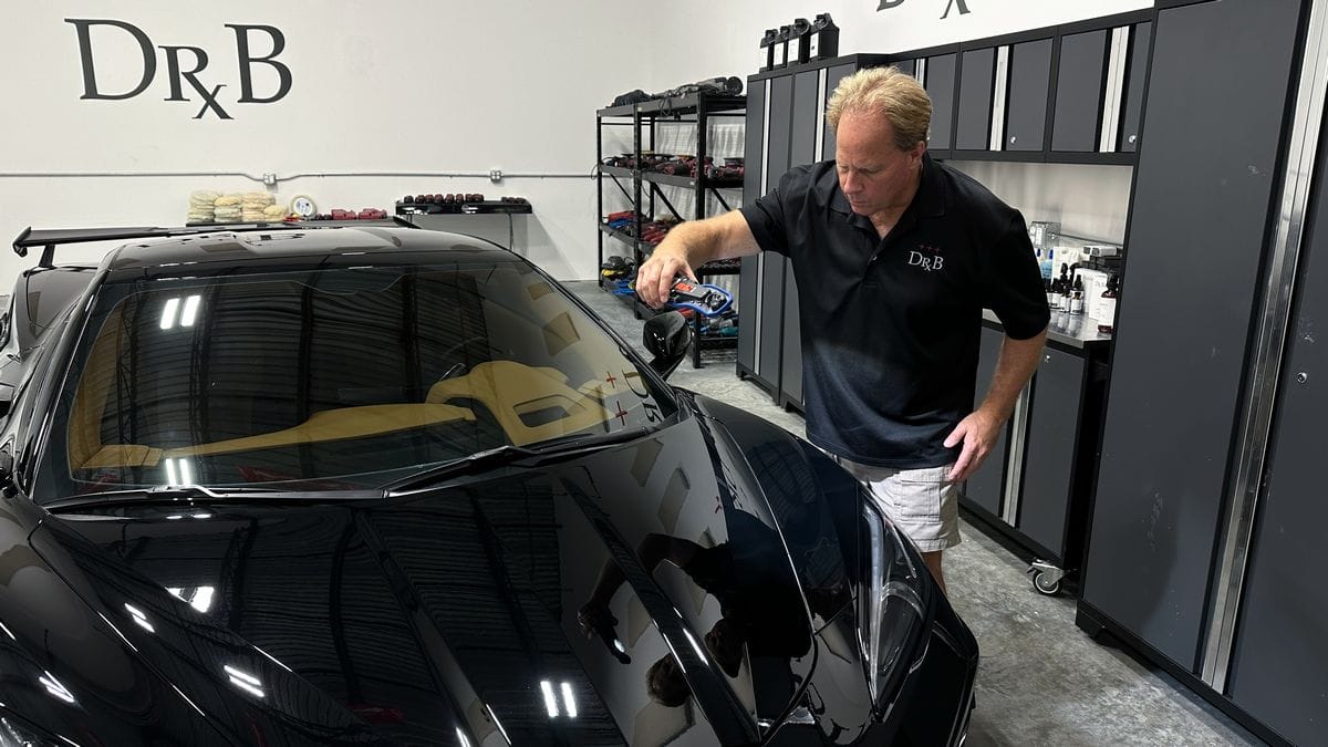 Mobil sport hitam yang sedang dipoles di bengkel detailing dengan kilau yang sangat jelas.