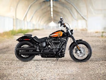Gambar Harley-Davidson Street Bob atau Fat Bob melaju di jalan pantai yang indah di Bali, menekankan posisi berkendara yang santai dan desain ikoniknya, dengan lanskap yang indah di latar belakang.