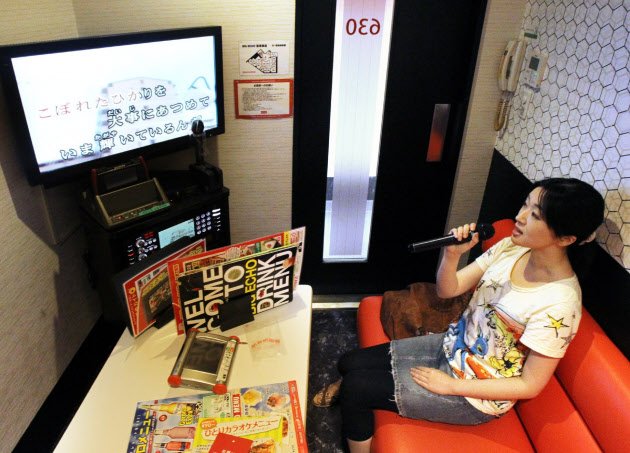 Sekelompok teman sedang bernyanyi ceria di ruangan karaoke sederhana K-Box Karaoke.