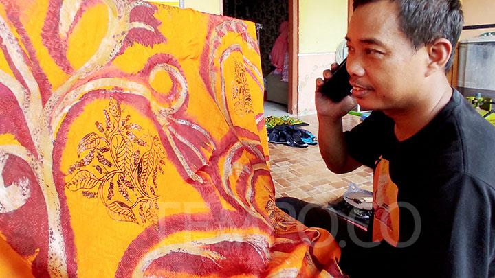 Seseorang sedang melukis pola di kain batik dengan canting di sebuah workshop membatik.