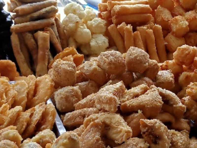 Aneka gorengan Indonesia (bakwan, tempe mendoan, pisang goreng) ditumpuk rapi di etalase penjual, siap saji.