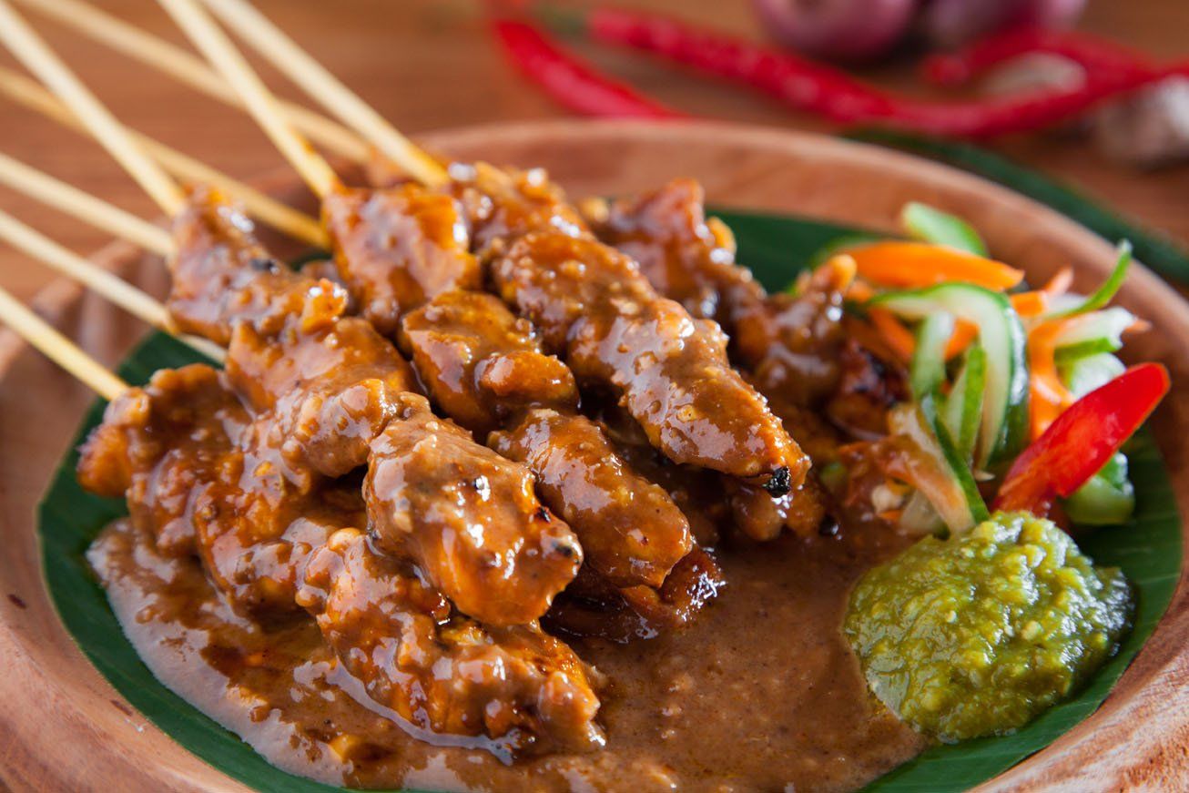 Sepiring sate ayam dengan bumbu kacang melimpah disajikan di warung kaki lima di malam hari.