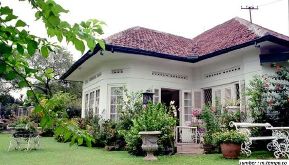 Gambar rumah bergaya kolonial dengan teras luas dan taman di daerah pegunungan yang sejuk.