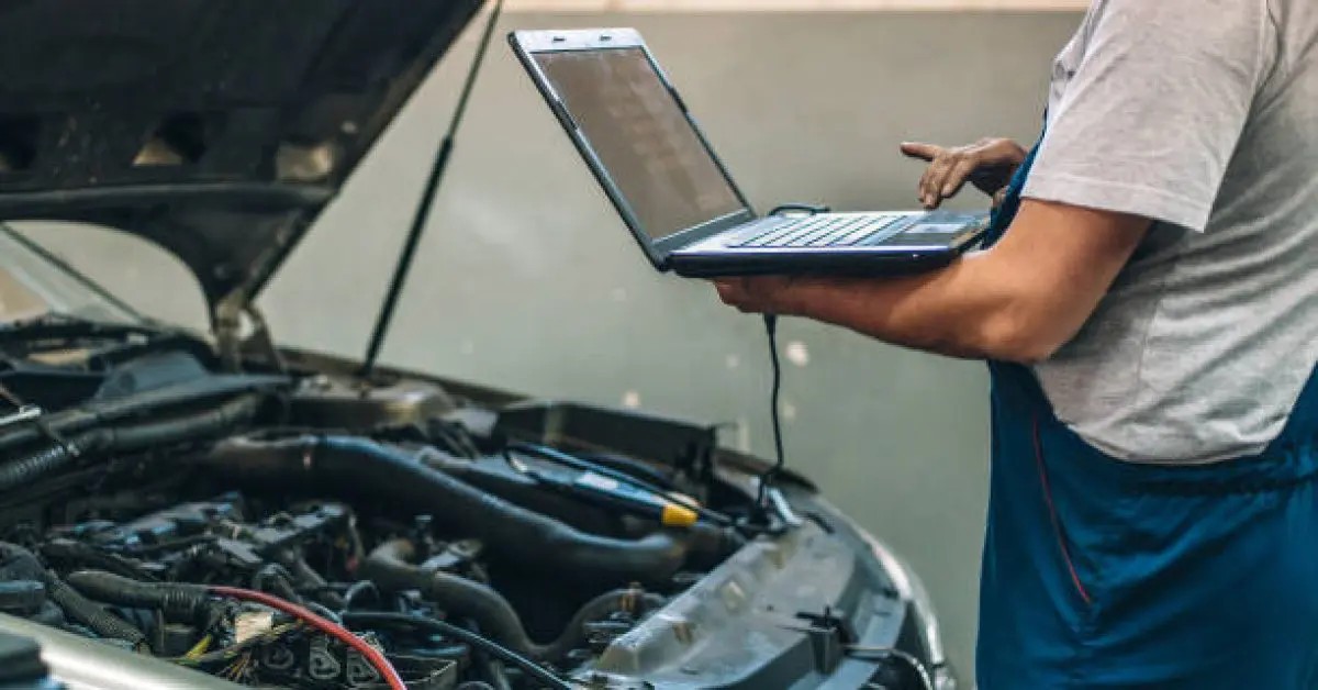 Mekanik sedang melakukan tune up mesin mobil dengan laptop diagnostik yang terhubung.