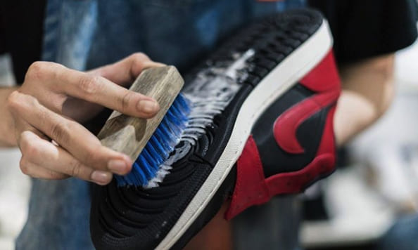 Sepatu sneakers sedang dibersihkan dengan kuas dan cairan khusus di Shoes and Care.