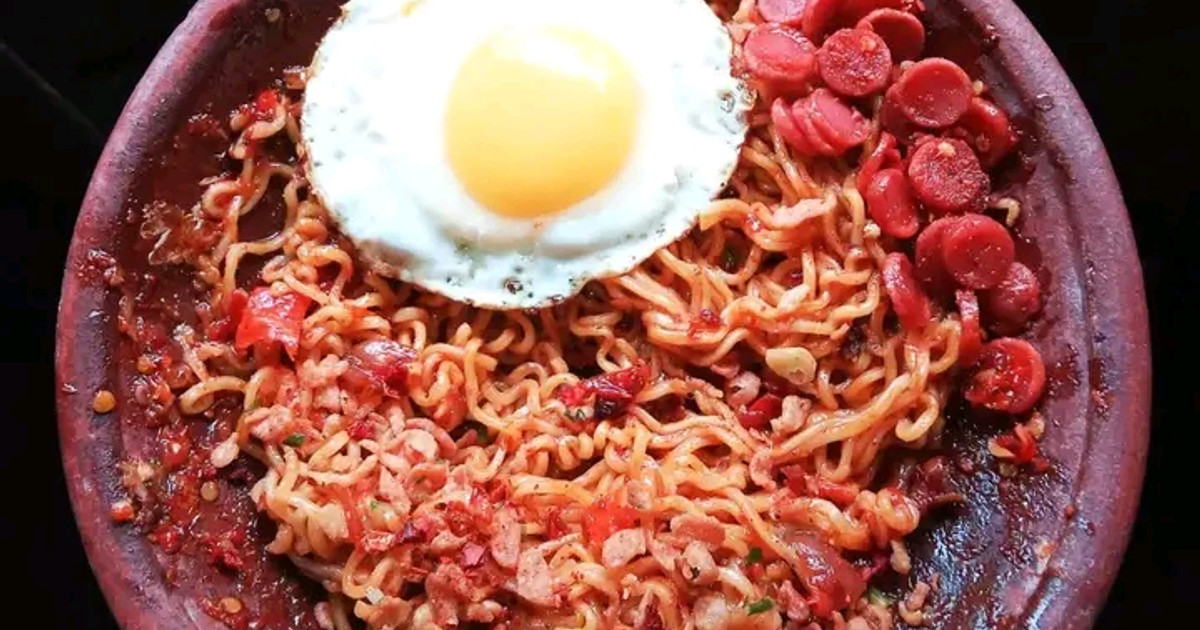 Semangkuk mie pedas dengan kuah merah dan topping cabai melimpah.