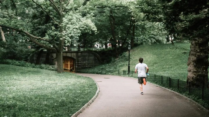 Orang sedang jogging di jalur hijau Hutan Kota Depok dengan pepohonan rindang.
