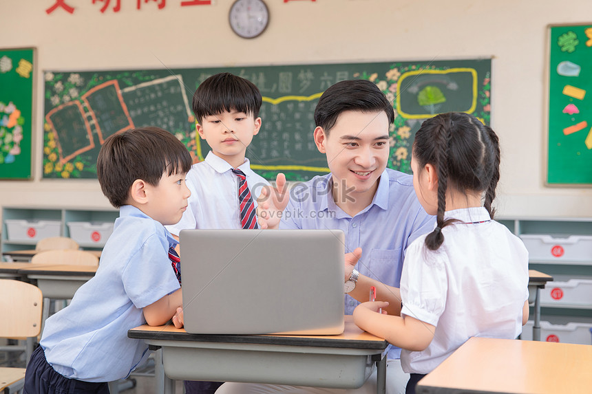 Gambar seorang siswa belajar mandiri dengan laptop di meja, sementara guru memberikan bimbingan pada siswa lain di dekatnya.