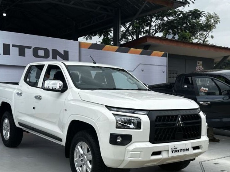 Gambar Mitsubishi Triton (kabin ganda) diparkir di lingkungan luar ruangan yang kasar atau lokasi konstruksi di dekat Makassar, menonjolkan bangunannya yang kokoh dan kegunaannya.