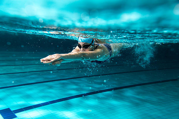 Gambar perenang sedang melakukan lap di kolam renang panjang berstandar olimpiade yang sepi.