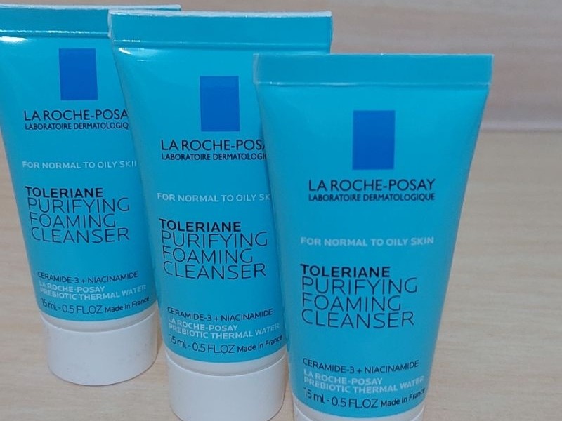 Gambar botol La Roche-Posay Toleriane Purifying Foaming Cleanser dengan desain estetika bersih dan medis, menonjolkan sifat menenangkan dan lembutnya, mungkin dengan tetesan air samar atau palet warna