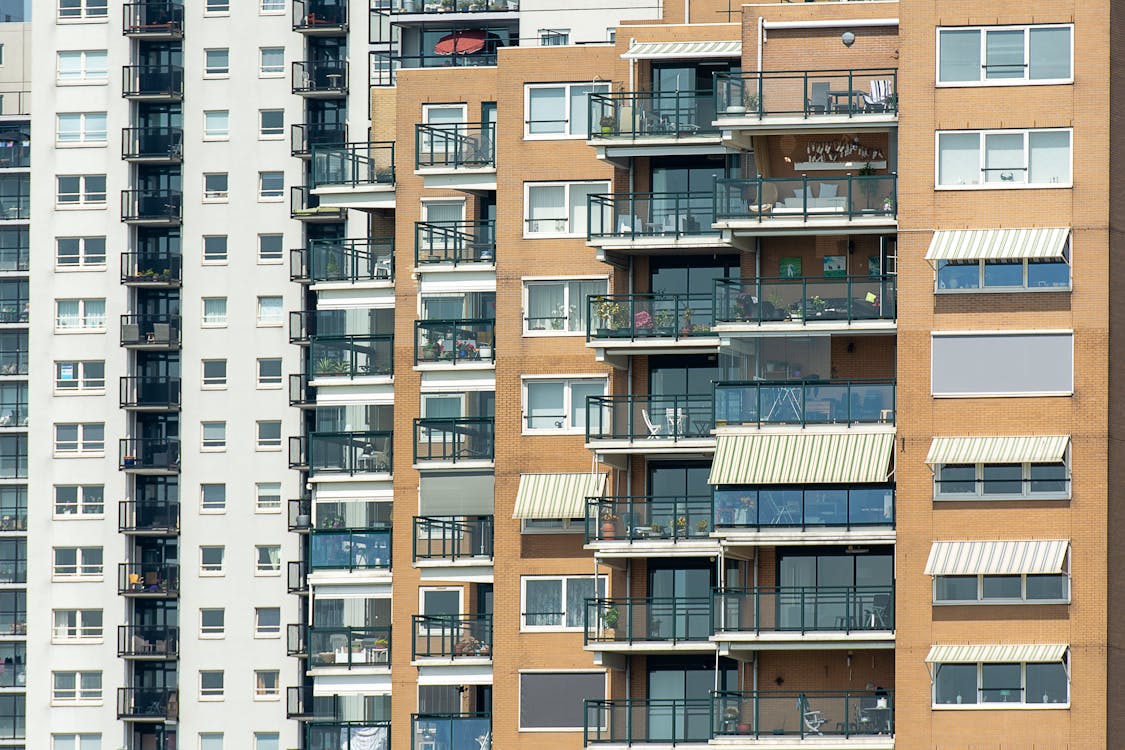 Gambar gedung apartemen modern tinggi dengan pemandangan kota dari balkon.