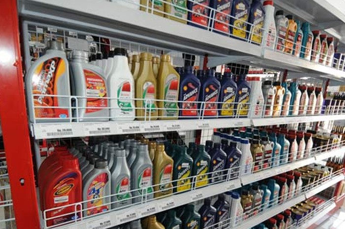 Botol-botol oli mesin dari berbagai merek yang tertata rapi di rak bengkel.
