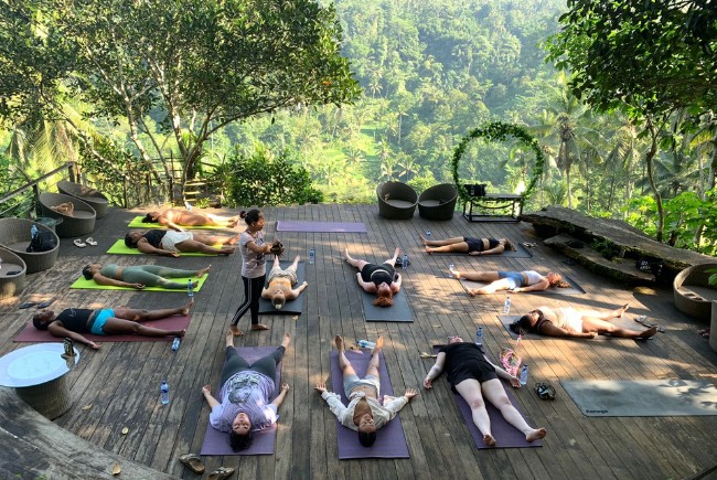 Area meditasi outdoor dengan matras yoga menghadap pemandangan hijau dan pepohonan rindang.