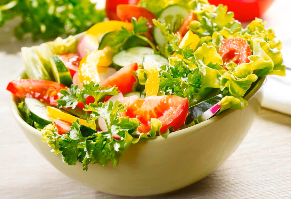 Semangkuk salad bowl dengan aneka sayuran hijau, buah, dan protein nabati.