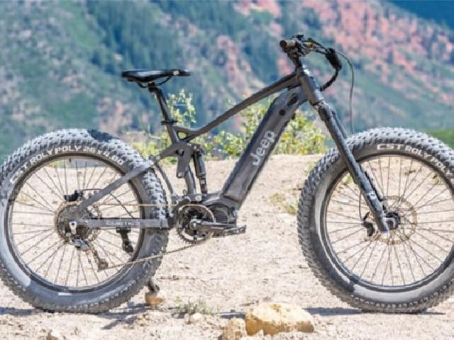 Gambar sepeda gunung elektrik Giant Trance E+ di jalur gunung yang menantang, dengan pengendara percaya diri mendaki lereng, menonjolkan bantuan elektriknya, dengan latar belakang samar lanskap alami 