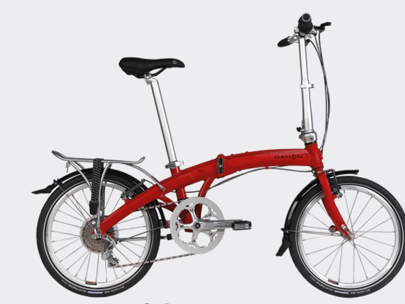 Gambar sepeda lipat Dahon Mu P8 terlipat diletakkan dengan elegan di samping meja kafe di lingkungan perkotaan, menonjolkan ukuran kompak dan nuansa premiumnya, dengan latar belakang samar Jakarta Pus