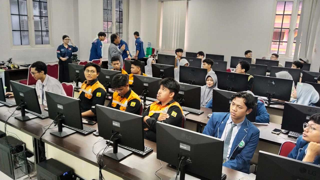 Mahasiswa sedang belajar coding di lab komputer dengan instruktur membimbing.