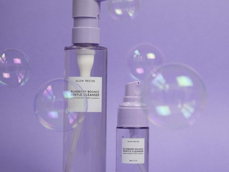 Gambar botol Glow Recipe Blueberry Bounce Gentle Cleanser dengan estetika cerah, ceria, dan bersih, menonjolkan bahan dasar buah dan sifat melembapkannya, dengan latar belakang samar Senayan City, Jak