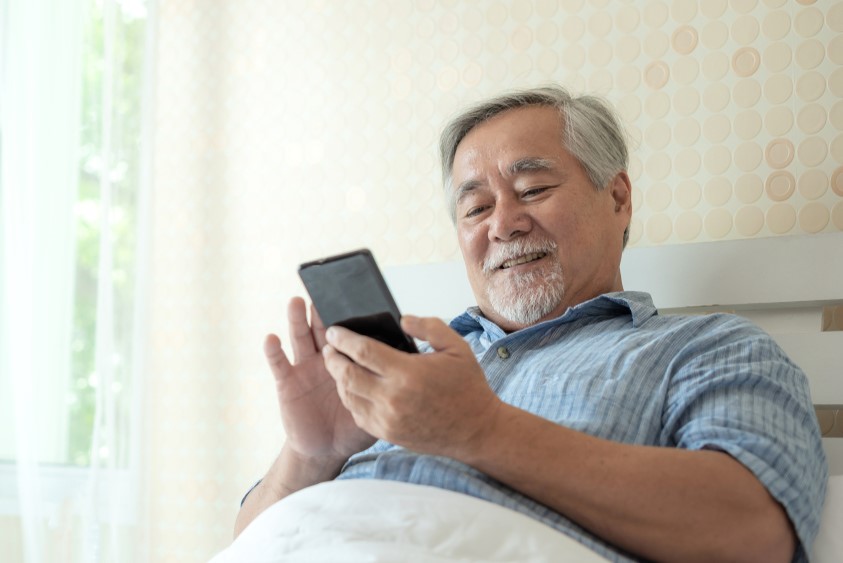 Seorang senior sedang tersenyum sambil menggunakan smartphone yang mudah digenggam.