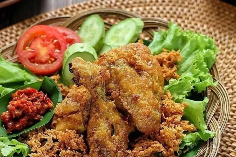Sepiring ayam goreng dengan kremesan, sambal, dan lalapan.