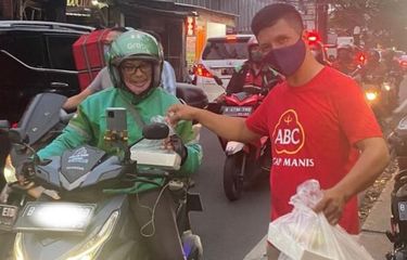 Seorang pengemudi ojol sedang menyantap seporsi nasi goreng di pinggir jalan.