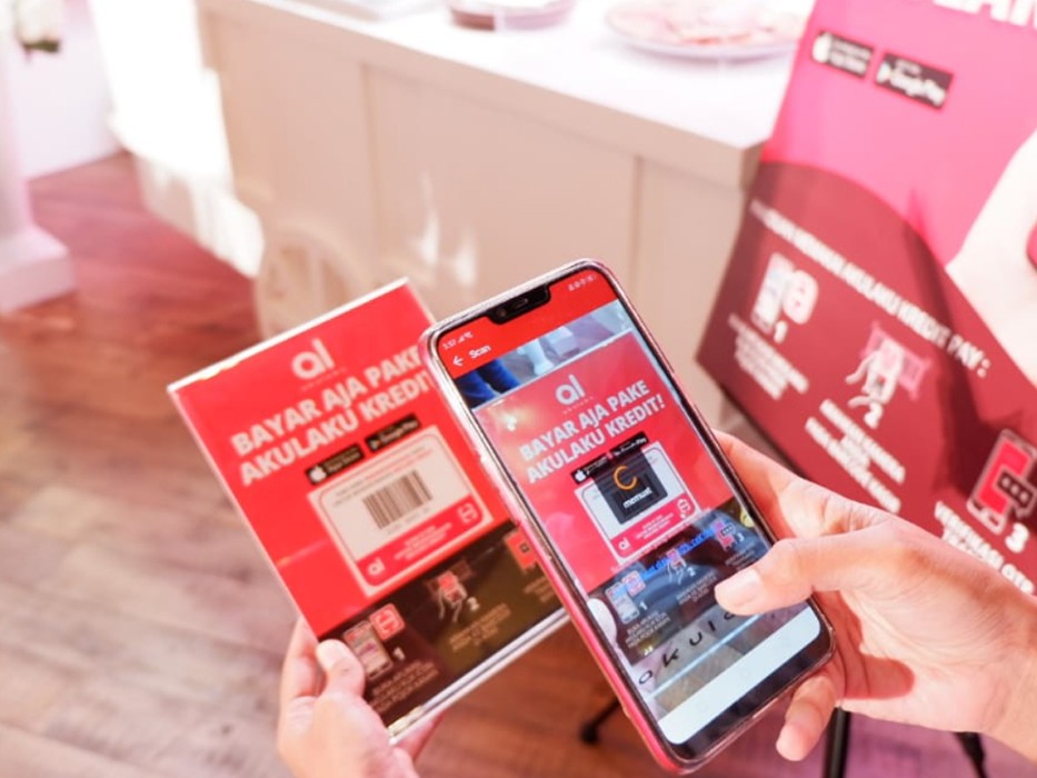  seseorang yang dengan senang hati membuka kotak gadget elektronik yang dibeli dengan Akulaku Paylater, dengan aplikasi Akulaku ditampilkan di smartphone terdekat,