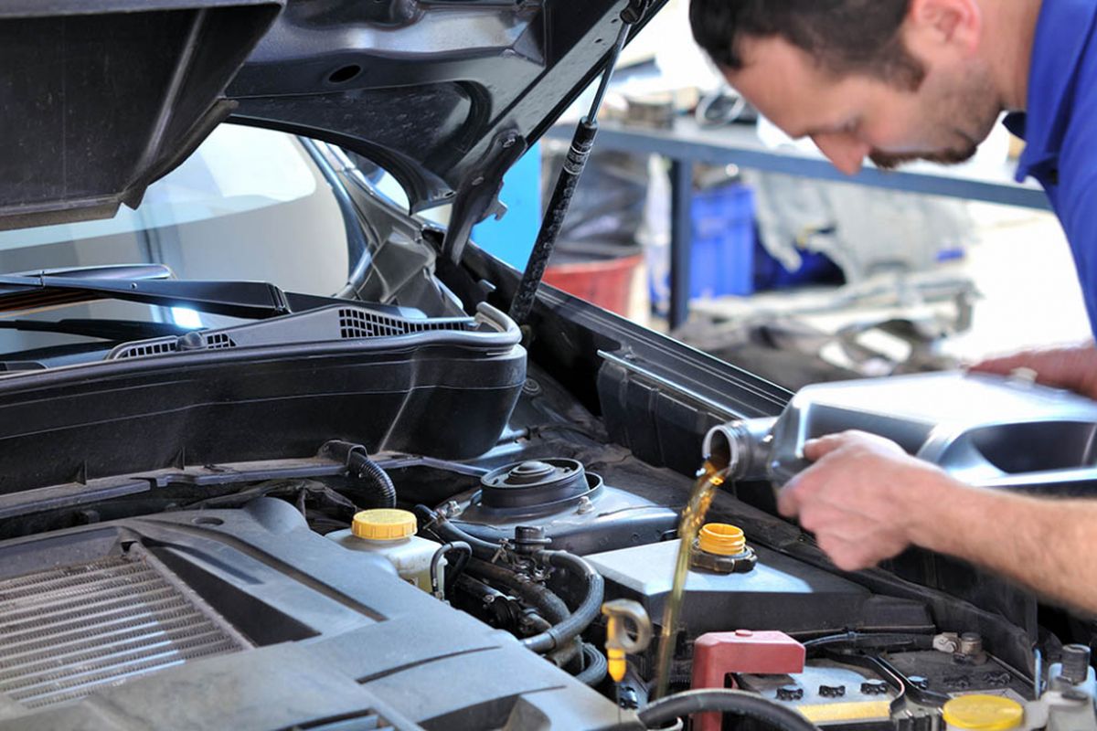 Teknisi sedang melakukan tune up pada mesin mobil dengan peralatan diagnostik.