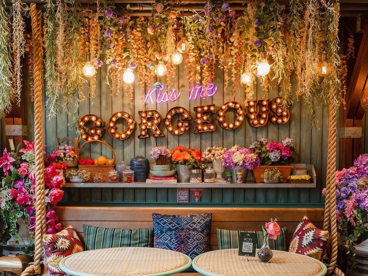 Interior cafe dengan dekorasi unik bertema taman fantasi, penuh bunga dan lampu.