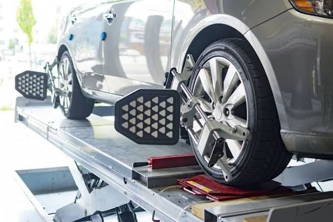 Mobil sedang dalam proses spooring menggunakan alat laser di bengkel yang bersih dan modern.