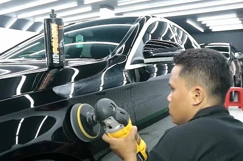 Seorang teknisi sedang mengaplikasikan cairan ceramic coating pada bodi mobil yang berkilau.