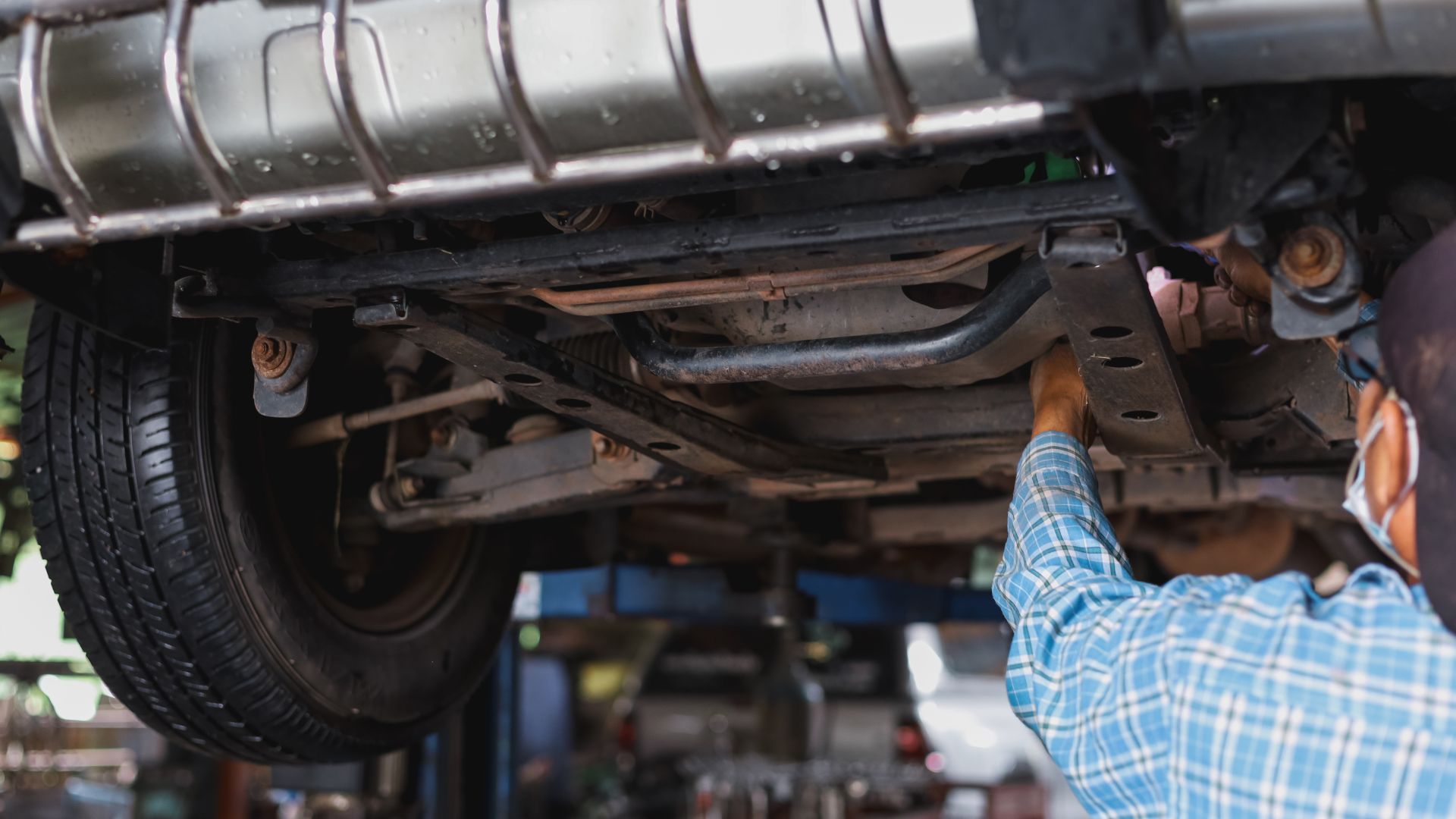 Montir sedang memeriksa sistem suspensi mobil di bengkel kaki-kaki.