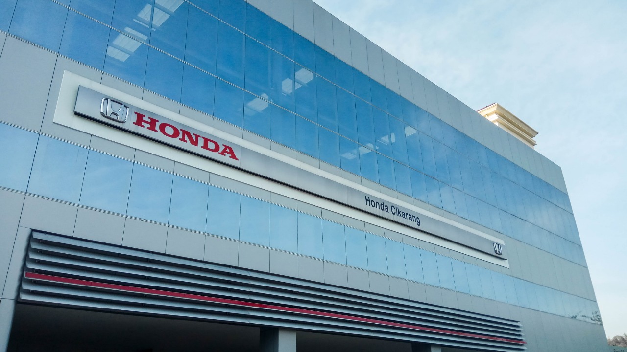 Gambar interior kantor modern dengan area khusus inspeksi motor, menampilkan seorang teknisi sedang memeriksa motor, mencerminkan kehadiran fisik sebuah marketplace online.