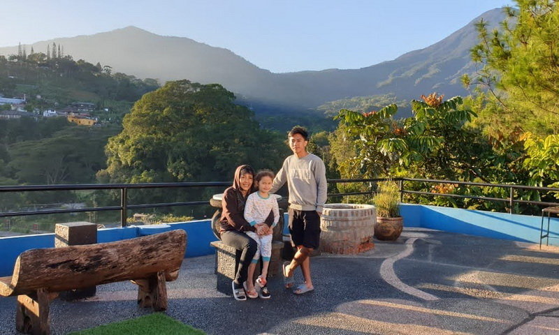 Rombongan orang berkumpul di halaman luas sebuah villa di Bogor dengan tenda dan area makan outdoor.