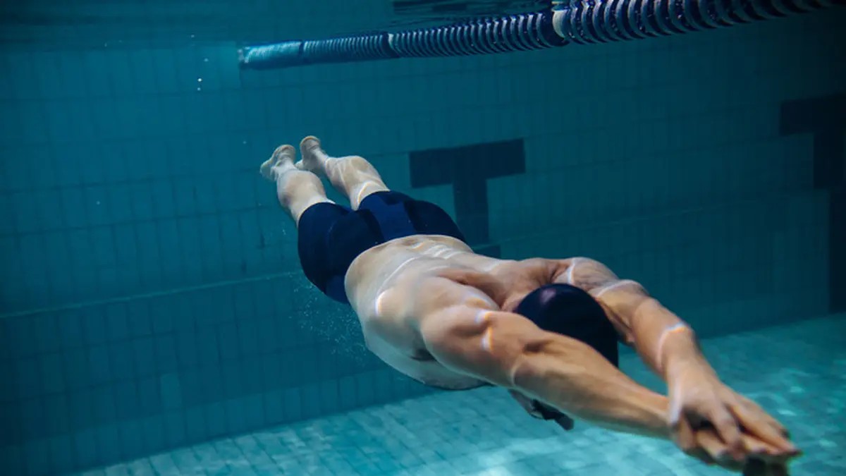 Gambar seorang perenang sedang melakukan gaya bebas di kolam renang yang panjang, terlihat serius berlatih.