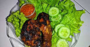 Potongan ayam bakar di piring dengan sambal terasi dan lalapan segar, terlihat bumbu yang meresap.