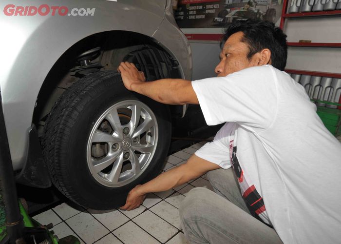 Mekanik sedang memeriksa sistem kaki-kaki mobil di bawah kolong mobil yang terangkat.