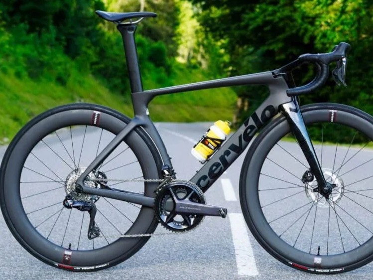 Gambar sepeda jalan Cervélo S5 di lintasan balap yang mulus atau jalan lebar dan terbuka, menonjolkan profil aerodinamis dan rampingnya, dengan latar belakang samar Jakarta Selatan.