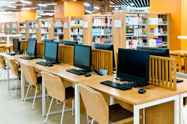 Gambar perpustakaan sekolah modern dengan meja belajar individual dan komputer yang bersih.